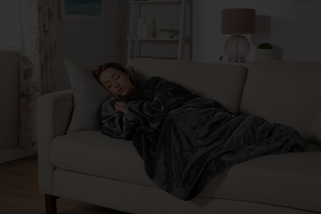 Femme enveloppée dans un plaid doux Softncosy sur un canapé, ambiance refuge cocooning à la maison